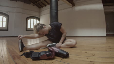 Long-shot-of-female-kickboxer-stretching-legs-on-floor-in-gym
